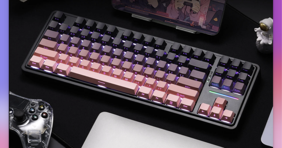 The image features a mechanical keyboard with a gradient keycap design, transitioning from black to pink, with purple backlighting. The keyboard is placed on a black desk mat, with a transparent game controller to the left and a silver laptop to the right. A tablet displaying an anime scene is propped up in the background. A small astronaut figurine is visible on the right side of the keyboard. The overall setup suggests a gaming or creative workspace.
