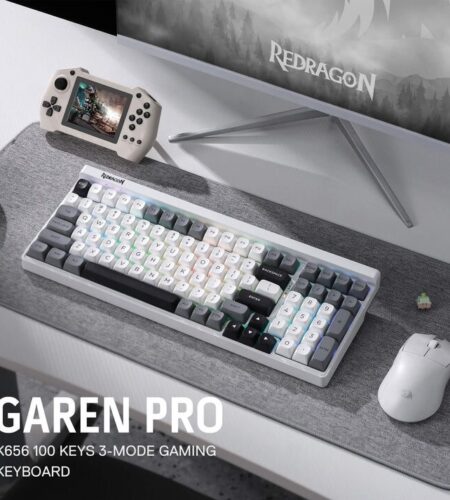 A product shot displays a white gaming keyboard, mouse, and controller, arranged on a desk in front of a computer monitor. The keyboard is positioned centrally, showing its layout with visible keys and a silver trim. To the right of the keyboard is a white wireless mouse, and to the left is a black gaming controller. The setup is placed on a dark-colored desk mat with a textured pattern, in front of a blurred computer monitor displaying a game scene. The text “GAREN PRO K656 100 KEYS 3-MODE GAMING KEYBOARD” is visible in large, bold letters on the bottom left corner of the image.