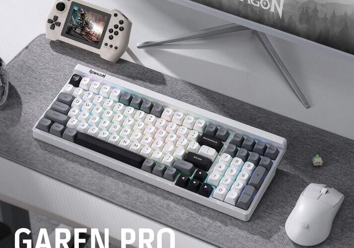 A product shot displays a white gaming keyboard, mouse, and controller, arranged on a desk in front of a computer monitor. The keyboard is positioned centrally, showing its layout with visible keys and a silver trim. To the right of the keyboard is a white wireless mouse, and to the left is a black gaming controller. The setup is placed on a dark-colored desk mat with a textured pattern, in front of a blurred computer monitor displaying a game scene. The text “GAREN PRO K656 100 KEYS 3-MODE GAMING KEYBOARD” is visible in large, bold letters on the bottom left corner of the image.