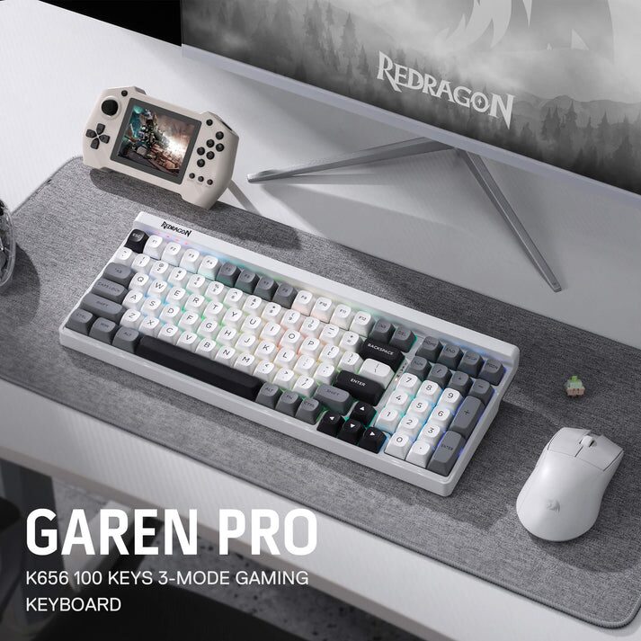 A product shot displays a white gaming keyboard, mouse, and controller, arranged on a desk in front of a computer monitor. The keyboard is positioned centrally, showing its layout with visible keys and a silver trim. To the right of the keyboard is a white wireless mouse, and to the left is a black gaming controller. The setup is placed on a dark-colored desk mat with a textured pattern, in front of a blurred computer monitor displaying a game scene. The text “GAREN PRO K656 100 KEYS 3-MODE GAMING KEYBOARD” is visible in large, bold letters on the bottom left corner of the image.