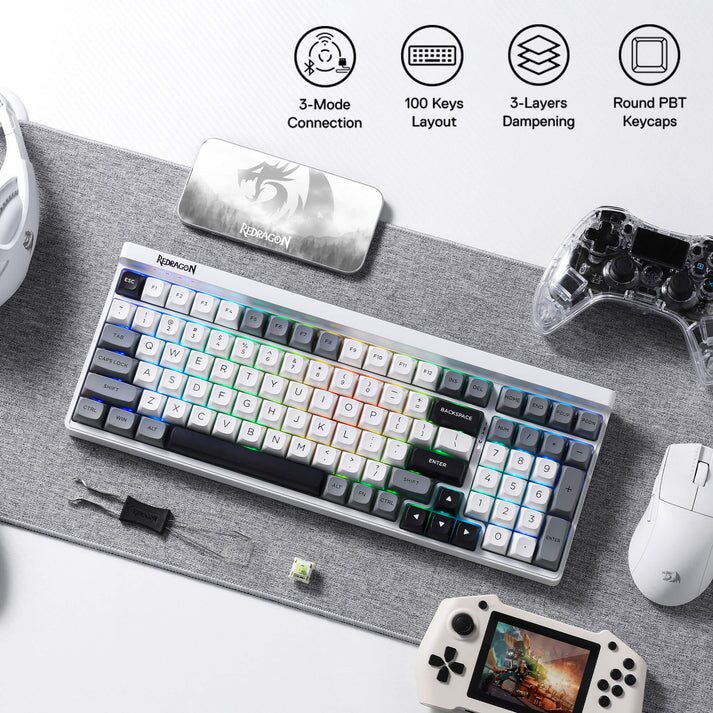The image displays a collection of gaming peripherals arranged on a red textured surface. The central focus is a white mechanical keyboard with RGB lighting, featuring a compact layout with alphanumeric keys, function keys, and a number pad. To the left of the keyboard is a white gaming mouse with additional buttons, and to the right is a white gaming controller. Above the keyboard is a long, rectangular black box with the word "REDDRAGON" printed in white. Four icons are positioned at the top corners of the image, stating “3-Mode Connection”, “100 Keys Layout”, “3-Layers Dampening”, and “Round PBT Keycaps”.
