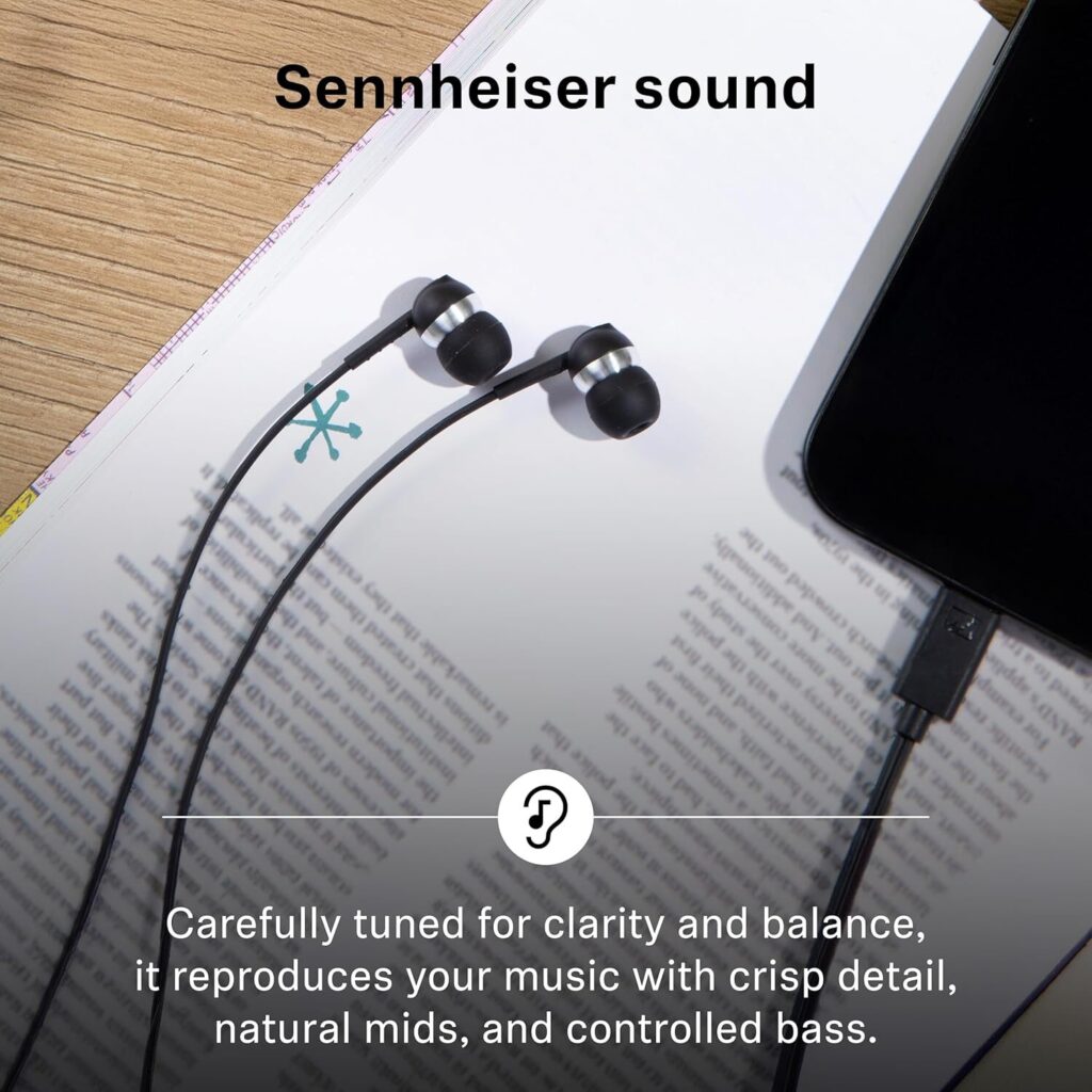 A top-down lifestyle photo of the Sennheiser CX 80U earbuds plugged into a smartphone, resting on an open book and a wooden desk. The earbuds are positioned near the center of the frame, showcasing their small, ergonomic form factor. Large bold text at the top reads "Sennheiser sound," and a caption at the bottom describes the audio profile as being "Carefully tuned for clarity and balance," featuring crisp detail, natural mids, and controlled bass.